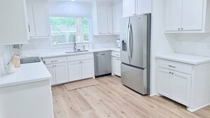 Una cocina moderna con armarios blancos, un refrigerador de acero inoxidable y una ventana con vistas a zonas verdes.