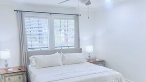 Un dormitorio con cama, mesitas de noche, ventilador de techo y ventana con persianas.