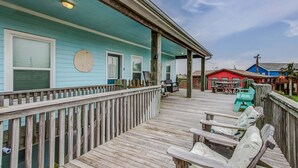 Eine Holzterrasse mit Sitzgelegenheiten im Freien, einem überdachten Bereich und einem Gebäude mit hellblau gestrichener Fassade.