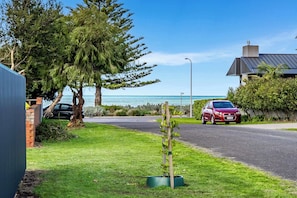 Une rue résidentielle où une voiture rouge est garée sur le bord, d’où l’on a une vue dégagée sur l’océan, et un immeuble avec un toit gris.