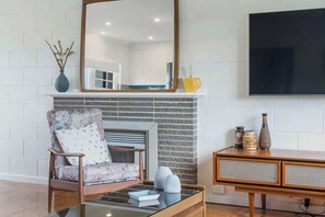 Un salon comprenant un canapé, une table basse, une cheminée, un miroir et un téléviseur fixé au mur.