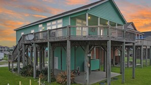 A two-story wooden structure with a balcony, a covered porch, and a satellite dish. - Mermaid Mansion 3 Bedroom Home (Port Bolivar)