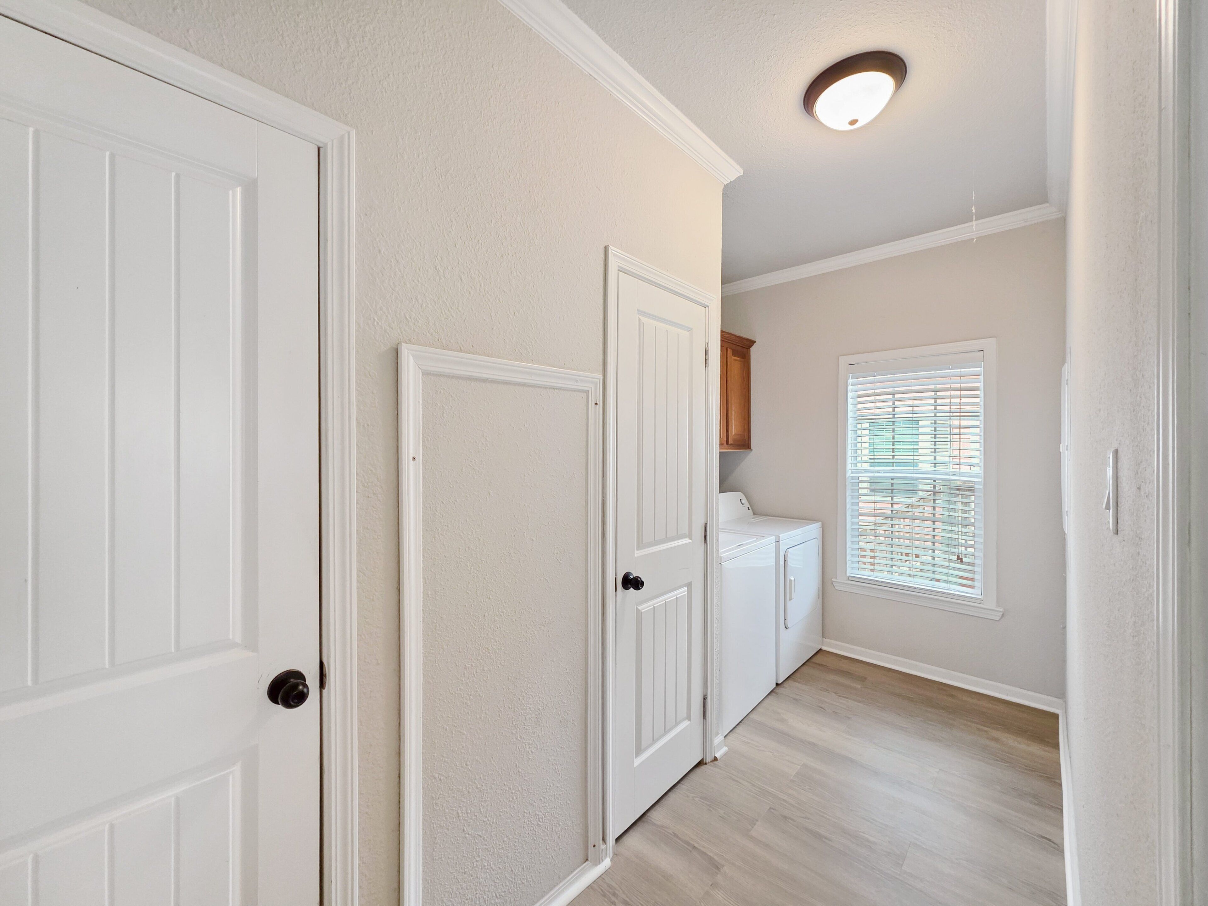 A hallway with white doors, a laundry area, and a window with blinds.