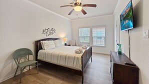 A bedroom with a bed, a ceiling fan, a TV, and a chair. - Mermaid Mansion 3 Bedroom Home (Port Bolivar)