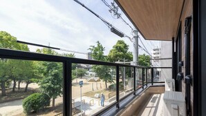 Ein Balkon mit Blick auf einen Park und Gebäude, mit Holzboden und Metallgeländer.