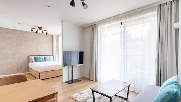 Ein modernes Hotelzimmer mit Bett, Fernseher, Sofa, Tisch und einem großen Fenster mit Vorhängen.