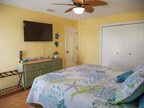 A bedroom with a bed, a ceiling fan, a TV, a dresser, and a door. - Sand in my boots - 2 Bedroom home in GULF SHORES with private pool and bikes (Gulf Shores)