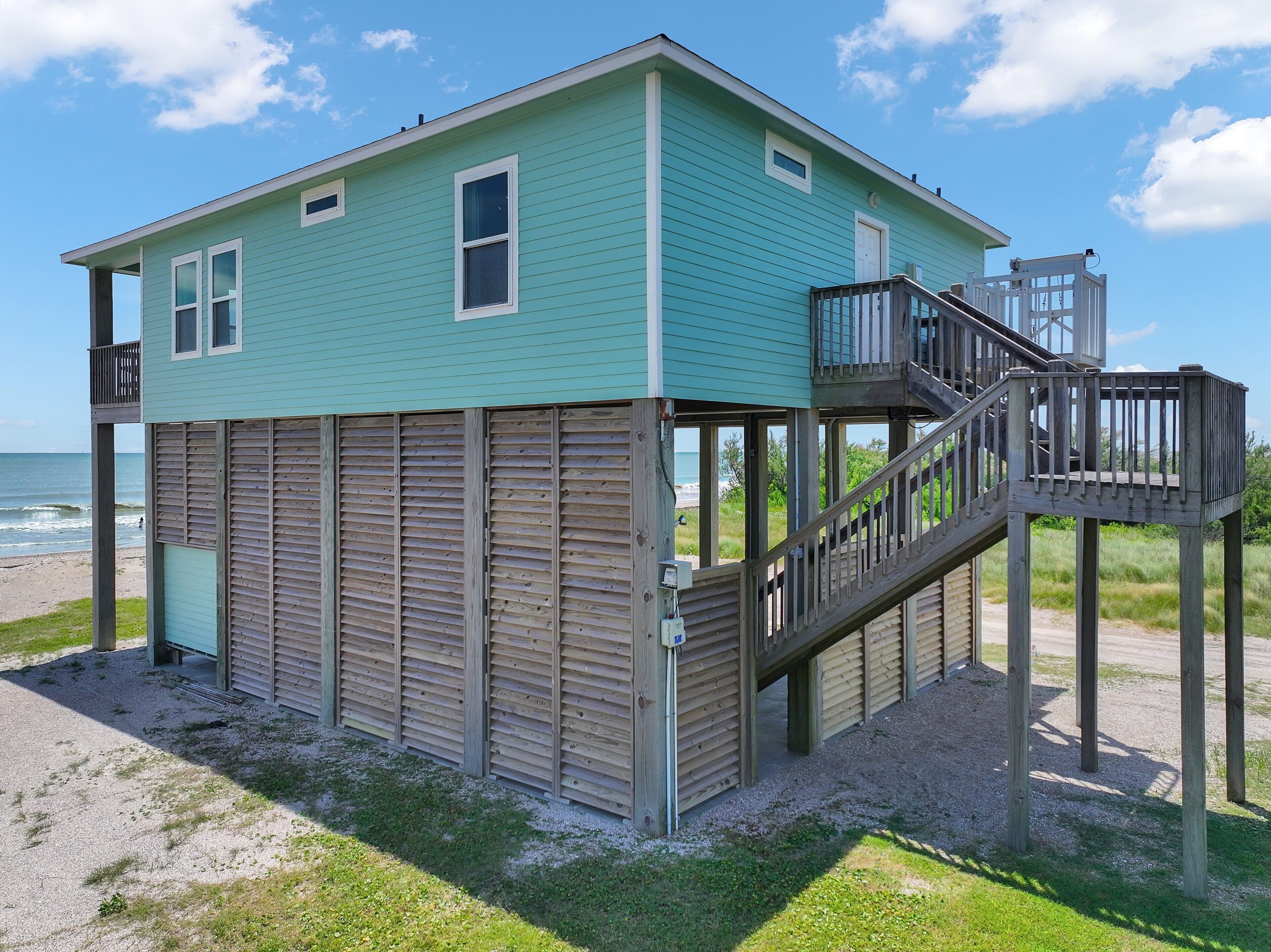 Een huis aan het strand met een houten terras, een trap en een klein balkon.