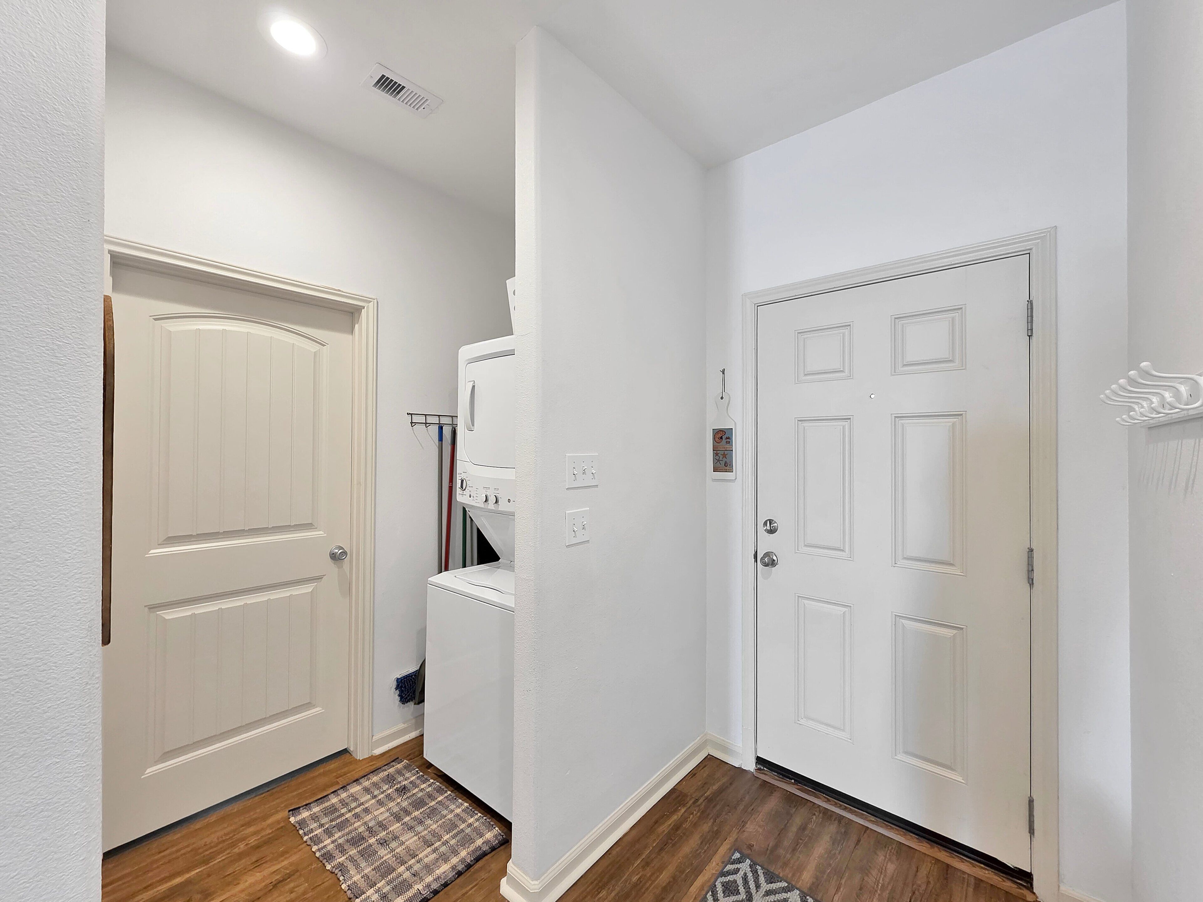 A hallway with a laundry area, a door with a decorative molding, and a patterned rug.