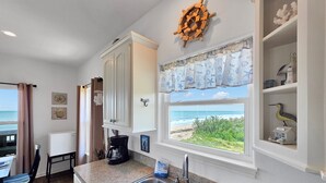 A kitchen with a view of the ocean, a coffee maker, and a ship's wheel decoration. - Sea Mist 2 Bedroom Home (Port Bolivar)