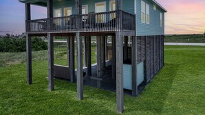 A two-story wooden house with a balcony, a covered patio, and a view of the surrounding landscape. - Sea Mist 2 Bedroom Home (Port Bolivar)