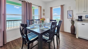 A dining area with a view of the ocean, a kitchen with white cabinets, and a dining table set for four. - Sea Mist 2 Bedroom Home (Port Bolivar)