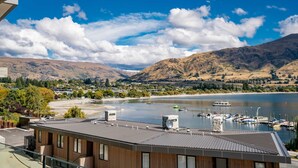 A modern building with a flat roof, a view of a lake with boats, and mountains in the background. - Lakeside Bliss Luxury 3 Bedroom Apartment (Wānaka)