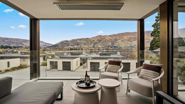 A modern balcony with a view of mountains, a sofa, two chairs, and a small table with a wine glass. - Lakeside Bliss Luxury 3 Bedroom Apartment (Wānaka)