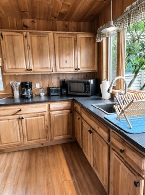 A kitchen with wooden cabinets, a microwave, a coffee maker, and a window with a view of greenery.