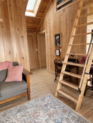 A wooden interior with a sofa, a ladder, and a patterned rug.