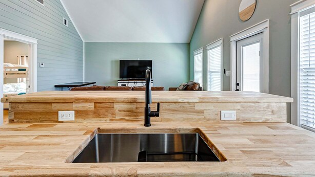 A modern kitchen with a large island, stainless steel sink, and a flat-screen TV. - Sea You Soon 2 Bedroom Home (Coffeyville)