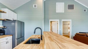 A modern kitchen with a wooden countertop, stainless steel appliances, and a view into the adjacent living area. - Sea You Soon 2 Bedroom Home (Coffeyville)