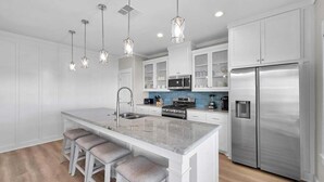 A modern kitchen with a central island, bar stools, stainless steel appliances, and pendant lighting. - Blue Anchor 5 Bedroom Home (Port Bolivar)
