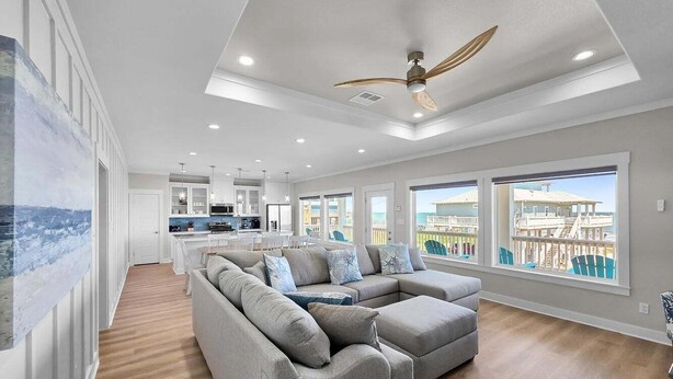 A spacious living room with a sectional sofa, a ceiling fan, and large windows offering a view of the outside. - Blue Anchor 5 Bedroom Home (Port Bolivar)