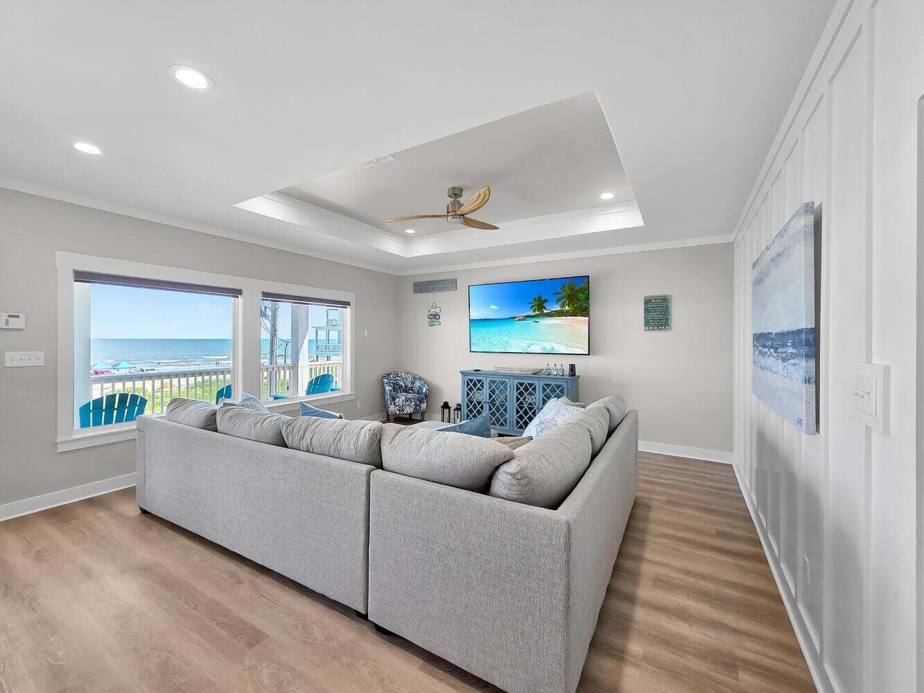 A modern living room with a large gray sectional sofa, a ceiling fan, and a view of the ocean through large windows.
