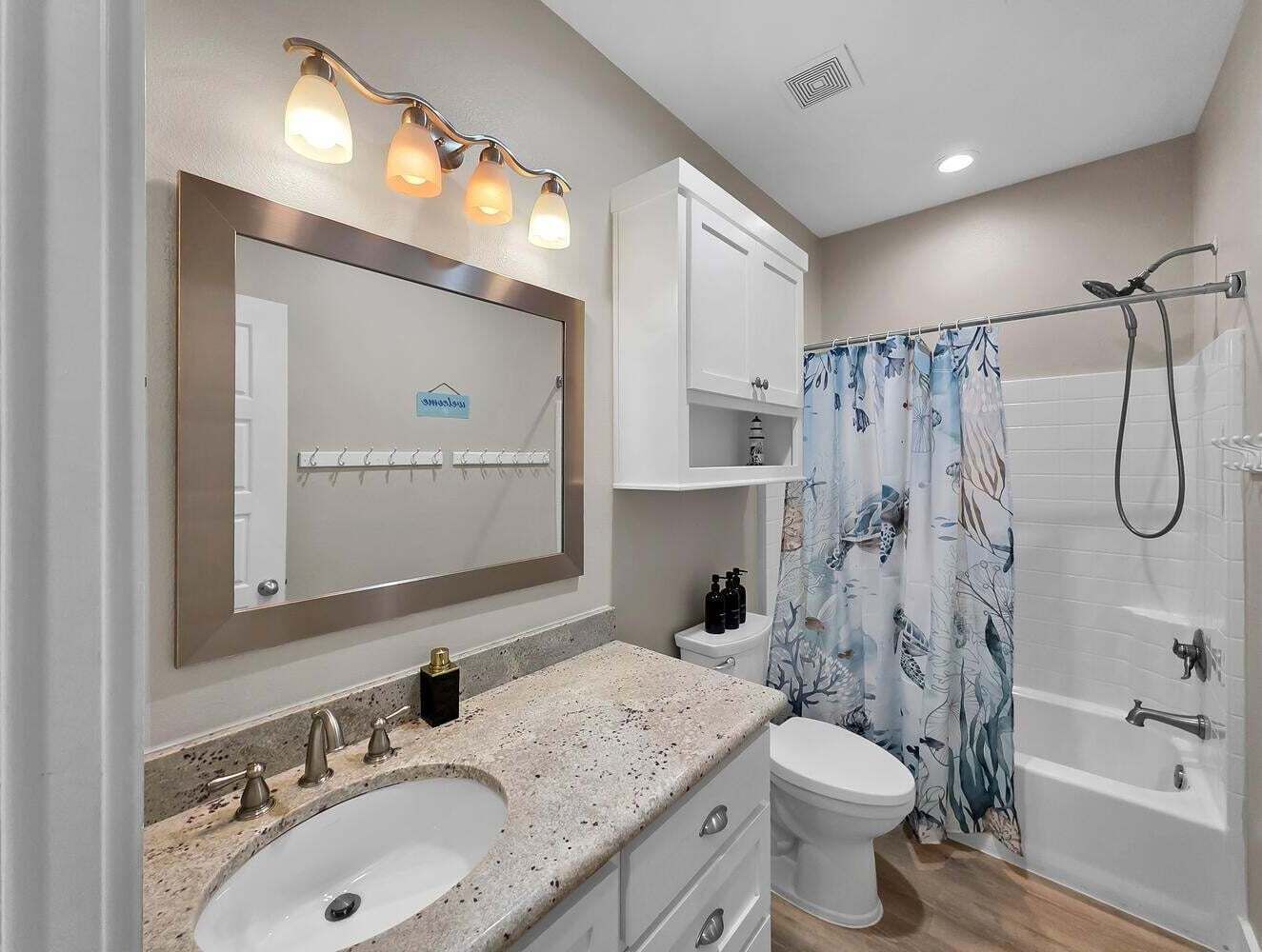 A bathroom with a large mirror, two sinks, a toilet, a shower with a curtain, and a cabinet above the toilet.