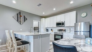 Una cocina moderna con armarios blancos, una isla central y un comedor con mesa de mármol.