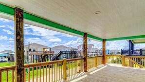 Una terraza de madera con barandillas, una vista despejada de casas al fondo y una viga estructural verde.