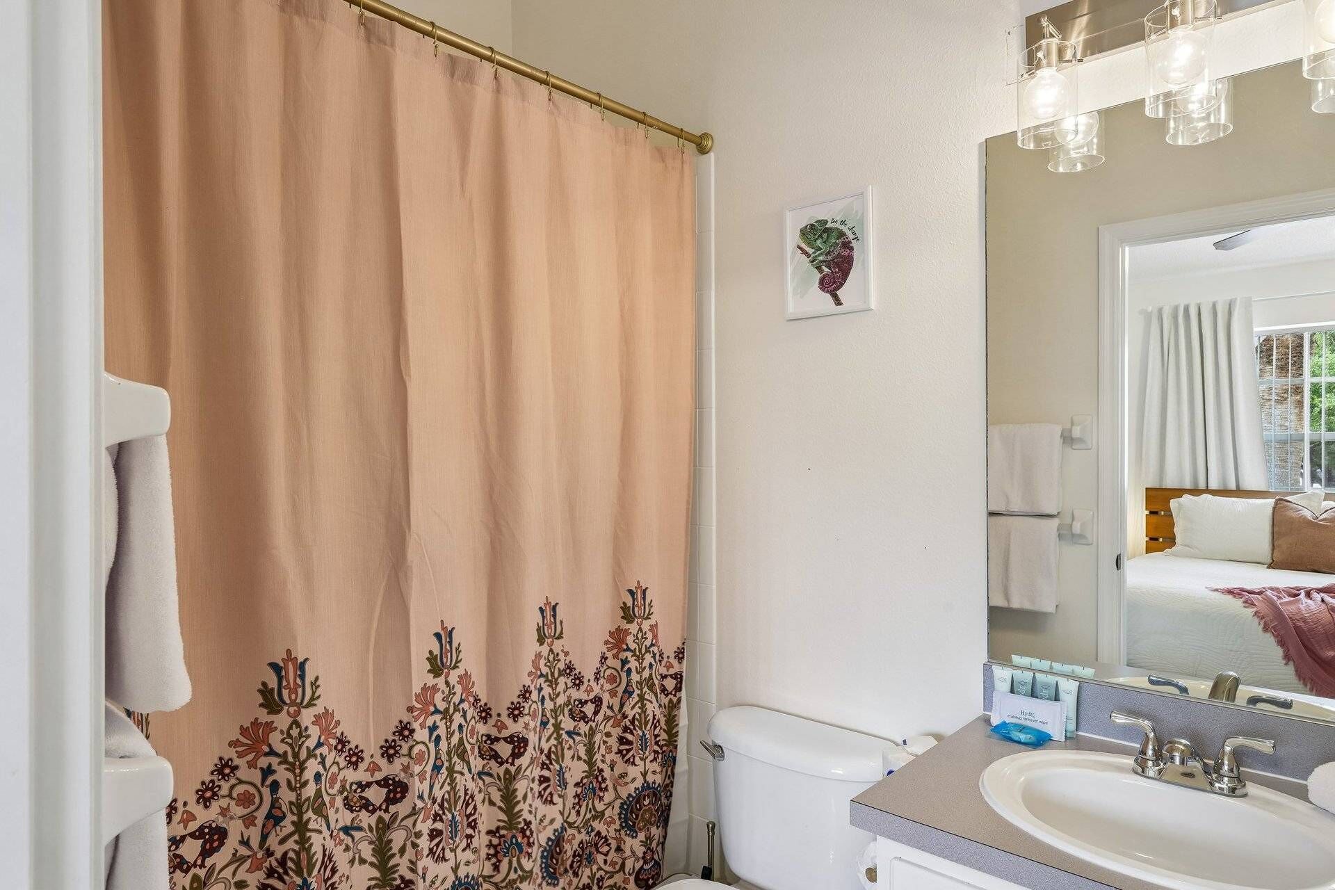 Ein Badezimmer mit Duschvorhang, Toilette, Waschbecken und Spiegel.