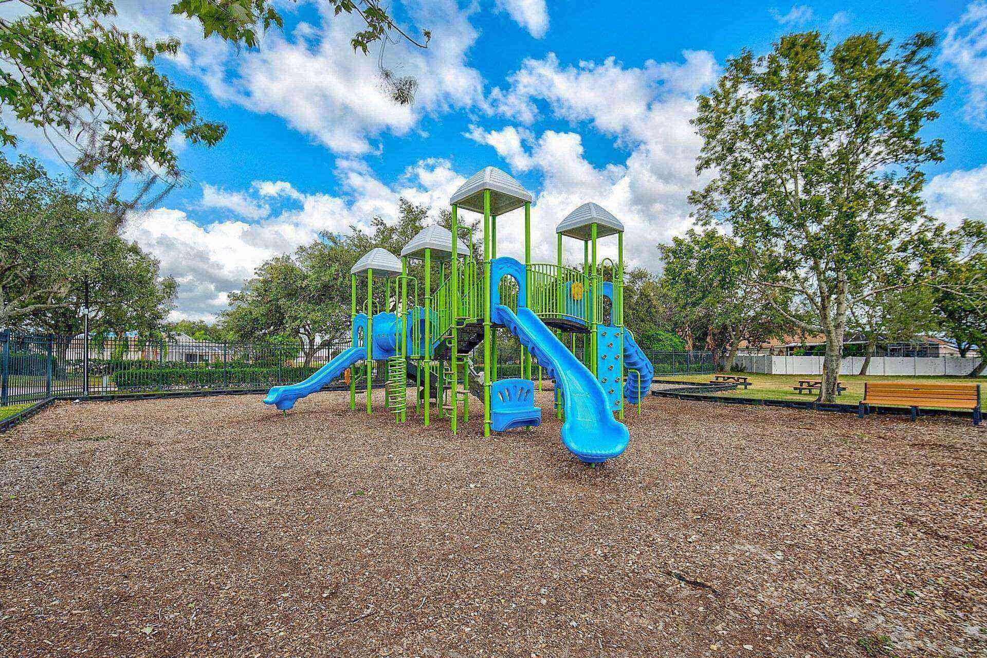 A playground with slides and climbing structures, surrounded by trees and a fence.