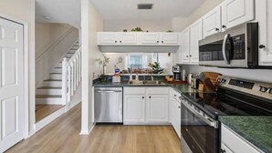 Une cuisine avec des meubles blancs, un four à micro-ondes, une cuisinière et un lave-vaisselle.