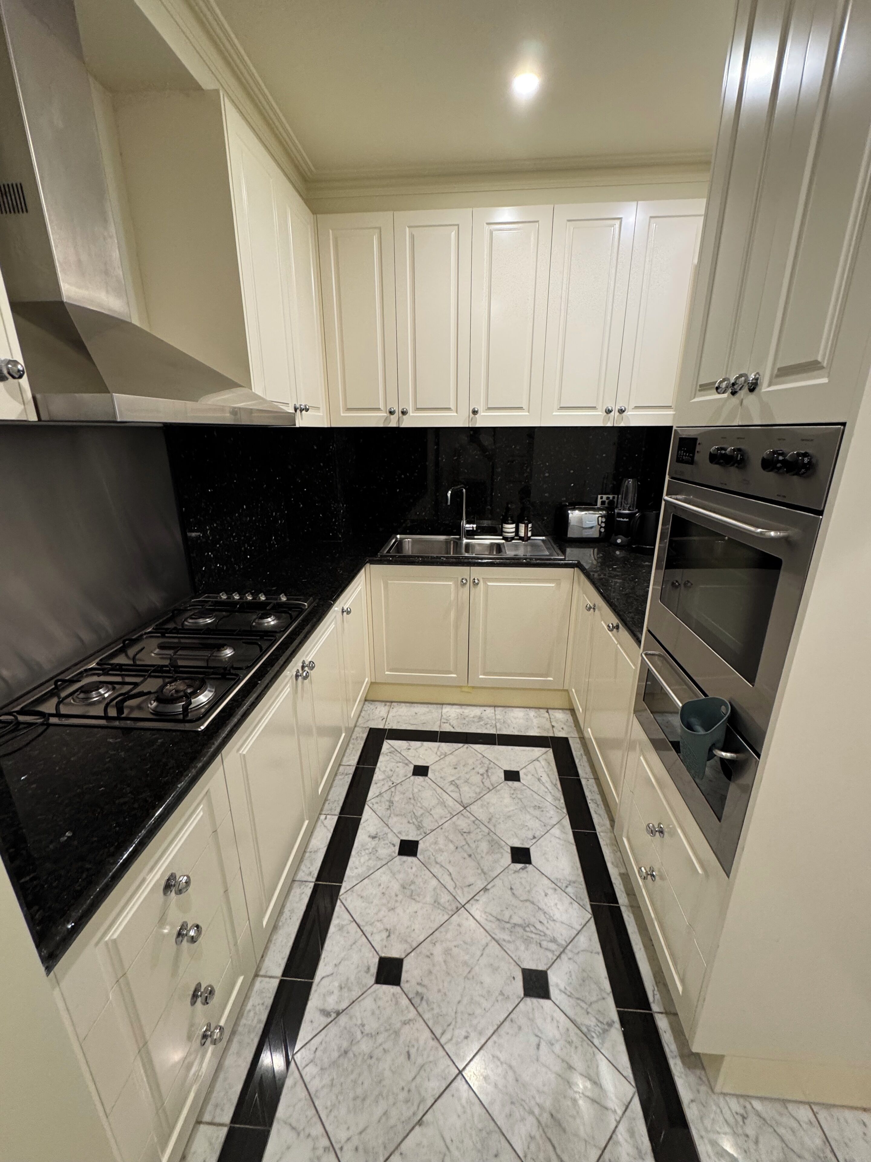 A modern kitchen with white cabinets, a black countertop, a gas stove, and a stainless steel oven.