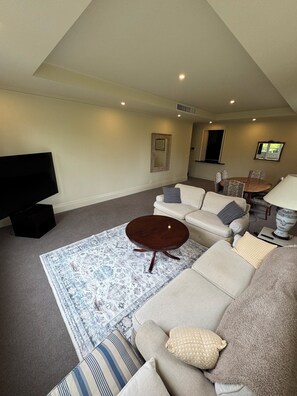 A living room with a sofa, a coffee table, a TV, and a patterned rug. - Luxury 3BR South Yarra Retreat Spa Bath BBQ & 2 Cars (South Yarra)
