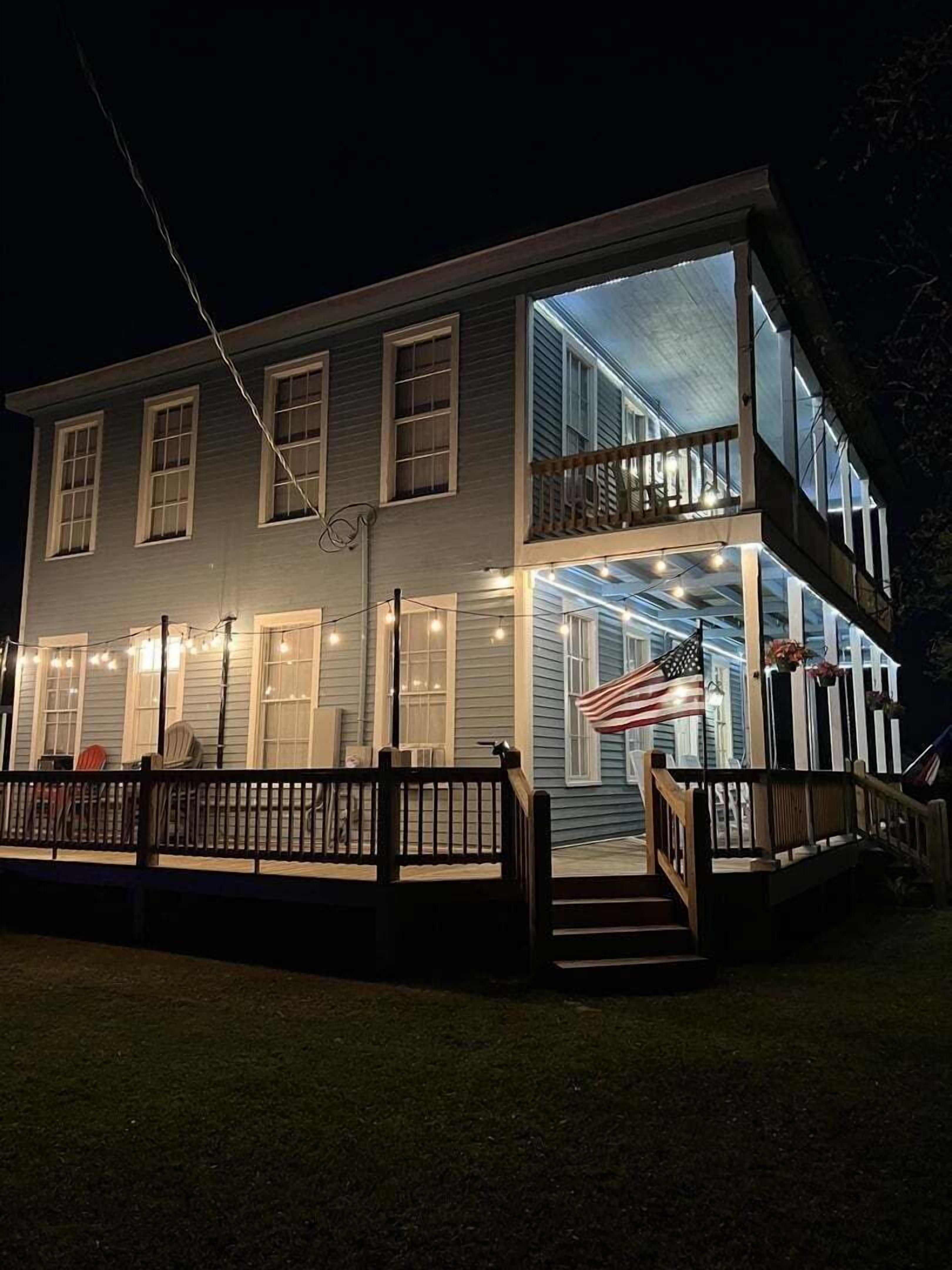 A two-story house with a balcony, a porch with string lights, and an American flag.
