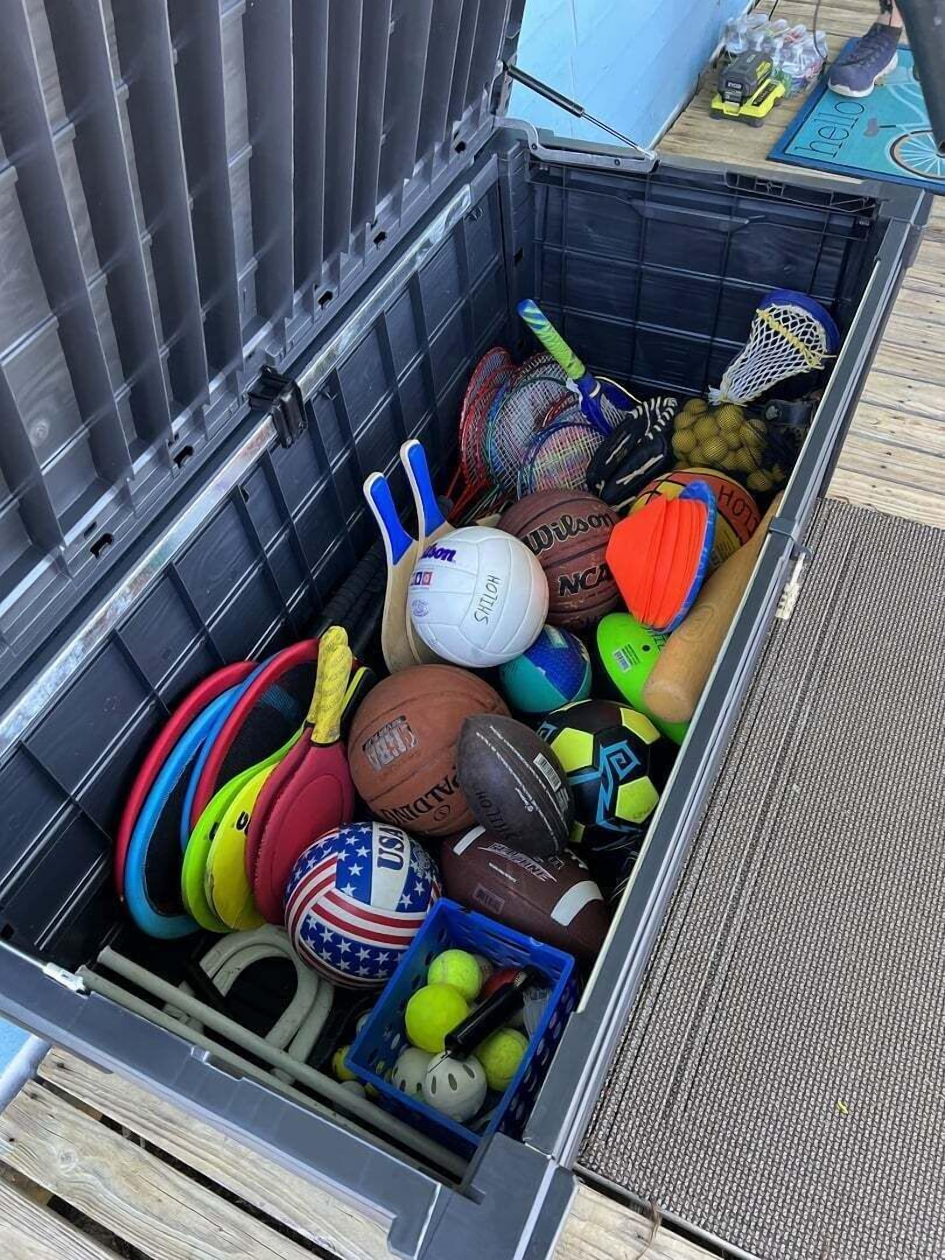 A storage container filled with various sports equipment including basketballs, volleyballs, and a tennis racket.