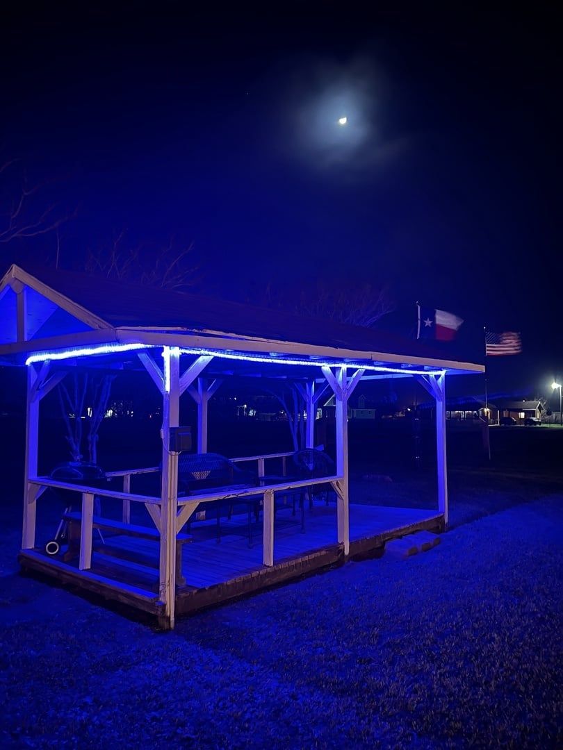 Une structure extérieure abritée, dotée d’un toit, qui pourrait être un gazebo ou un pavillon, et sur laquelle flotte un drapeau.