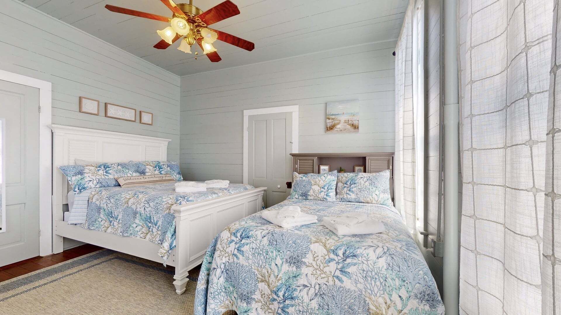 A bedroom with two beds, a ceiling fan, and a window with curtains.