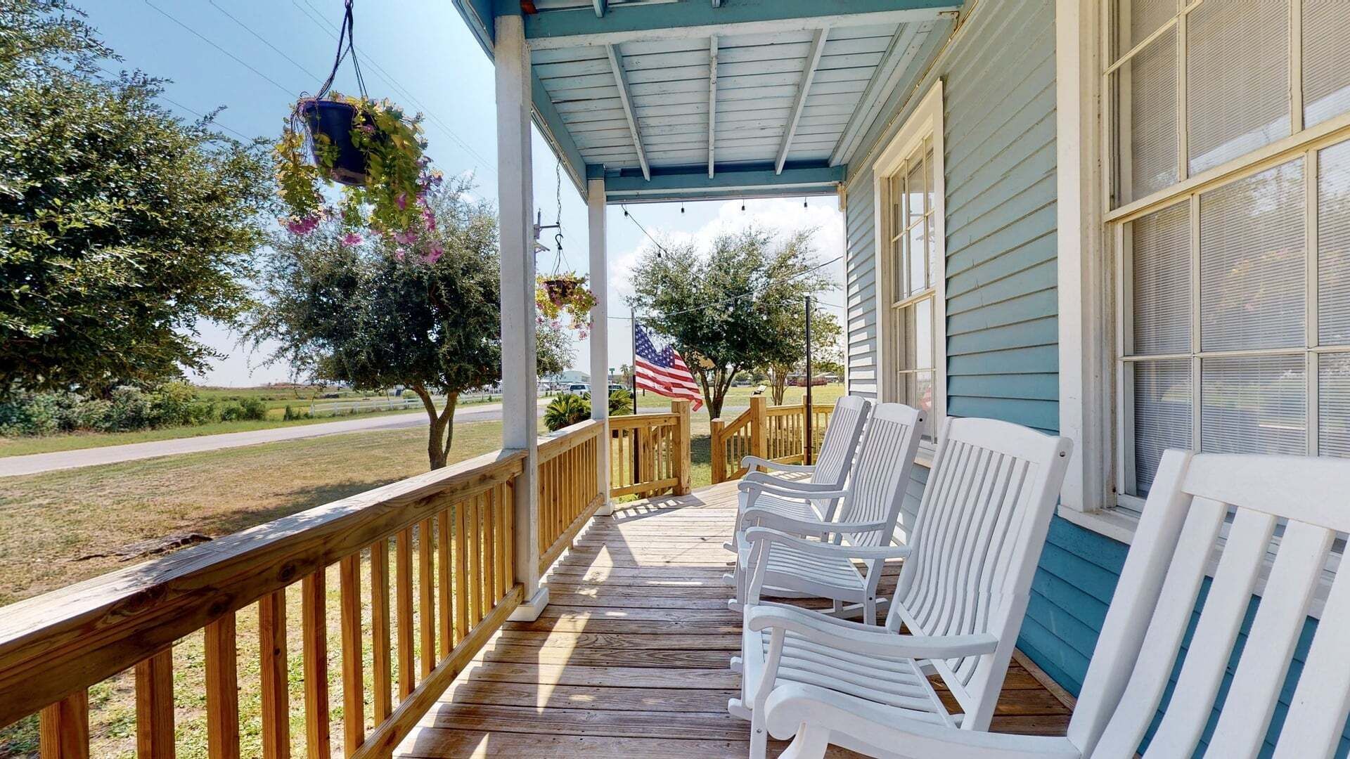 A covered porch with white chairs, a hanging flower pot, and an American flag.
