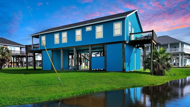 Un edificio de dos plantas con fachada azul y un porche cubierto, reflejado en el agua.