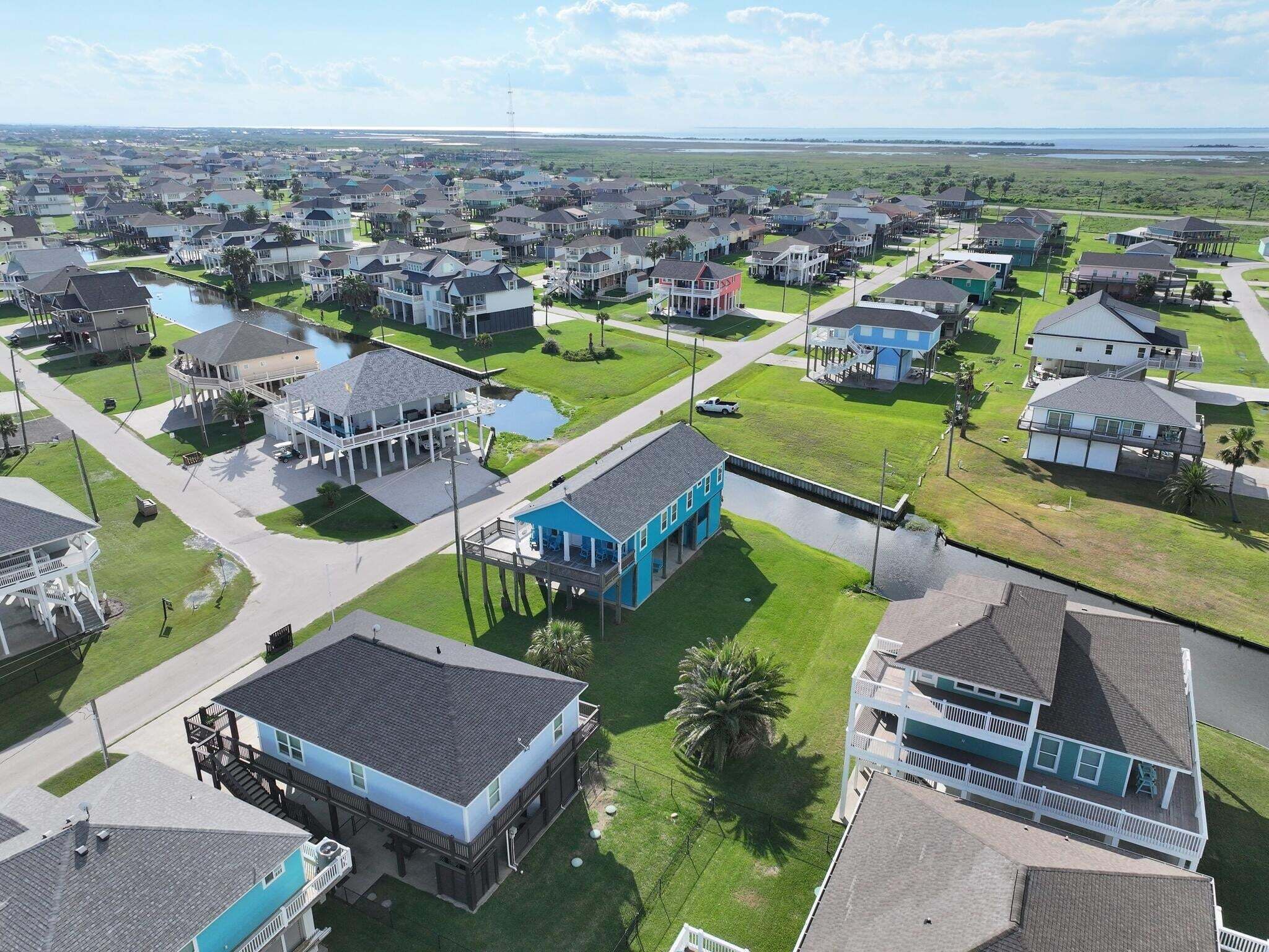 An aerial view of a residential area with houses, a water body, and a clear sky.
