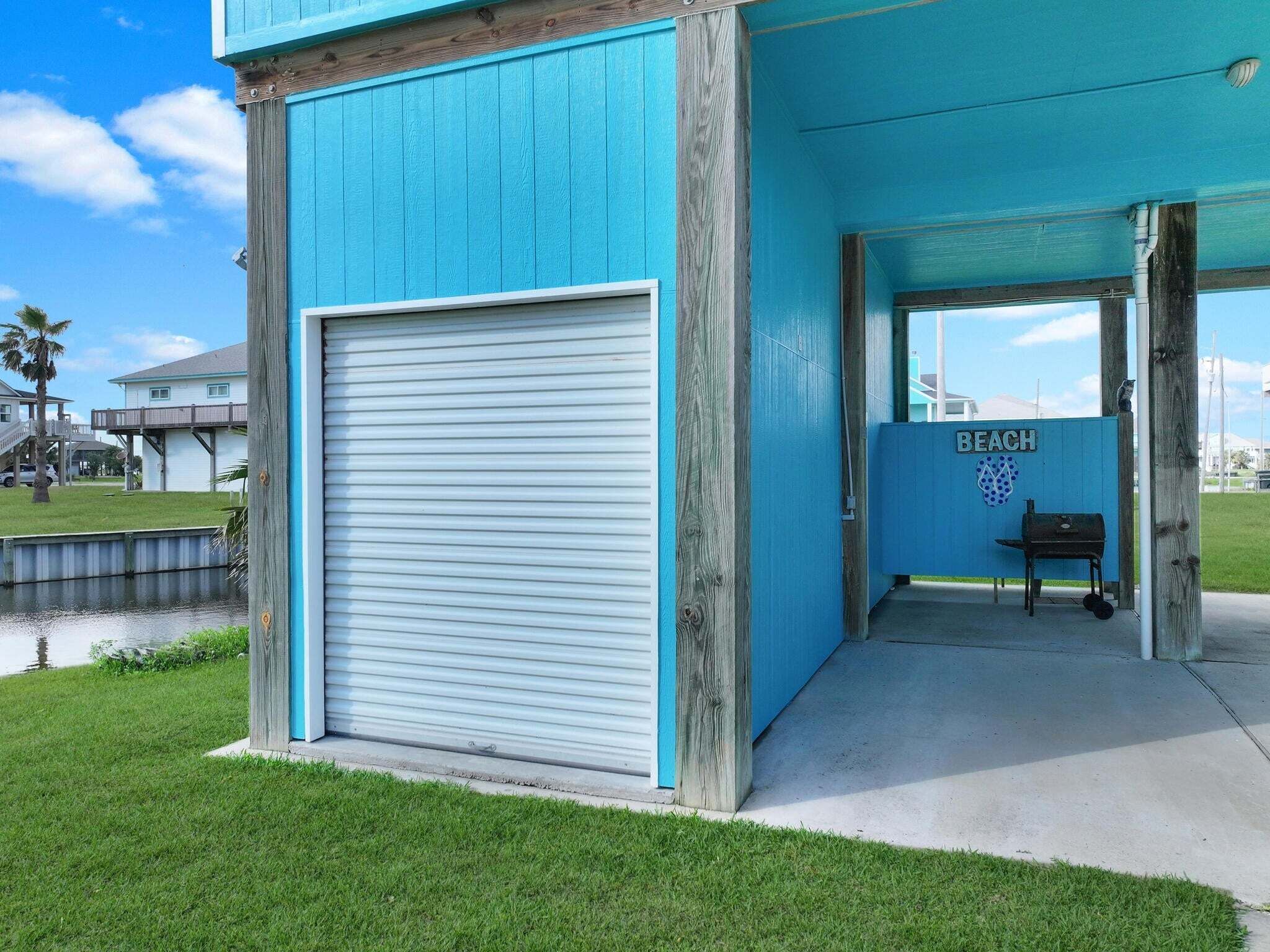 A blue building with a closed garage door, a bench, and a sign that reads 'BEACH'.