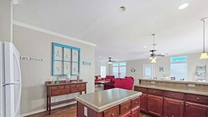 Una cocina con armarios de madera, una isla central y una zona de comedor con sillas rojas.