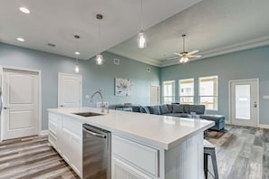 A modern kitchen with a large island, white cabinetry, and pendant lighting. - Jewel By The Sea 3 Bedroom Home (Port Bolivar)
