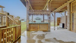 A wooden structure with a covered seating area, a lifebuoy, and a small building in the background. - Casa Siwichi 2 Bedroom Home (Port Bolivar)