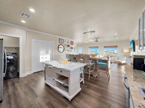 A spacious kitchen with a built-in island, a dining area with chairs, a ceiling fan, and a view through the windows. - Do Hideaway 3 Bedroom Home (Port Bolivar)