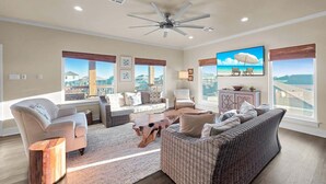 A spacious living room with a large window, a ceiling fan, and a flat-screen TV. - Do Hideaway 3 Bedroom Home (Port Bolivar)