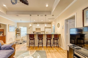 A modern kitchen with bar stools, a dining area with a table and chairs, and a living room with a sofa and TV. - Sharkyfin's Ii 3 Bedroom Home (Port Bolivar)