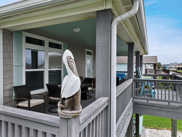 A covered outdoor area with a seating arrangement, a decorative bird sculpture, and a view of the surrounding neighborhood. - Turtle Beach 3 Bedroom Home (Port Bolivar)