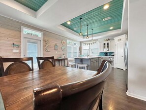 A modern kitchen with a wooden dining table, white cabinets, and a teal ceiling. - Turtle Beach 3 Bedroom Home (Port Bolivar)