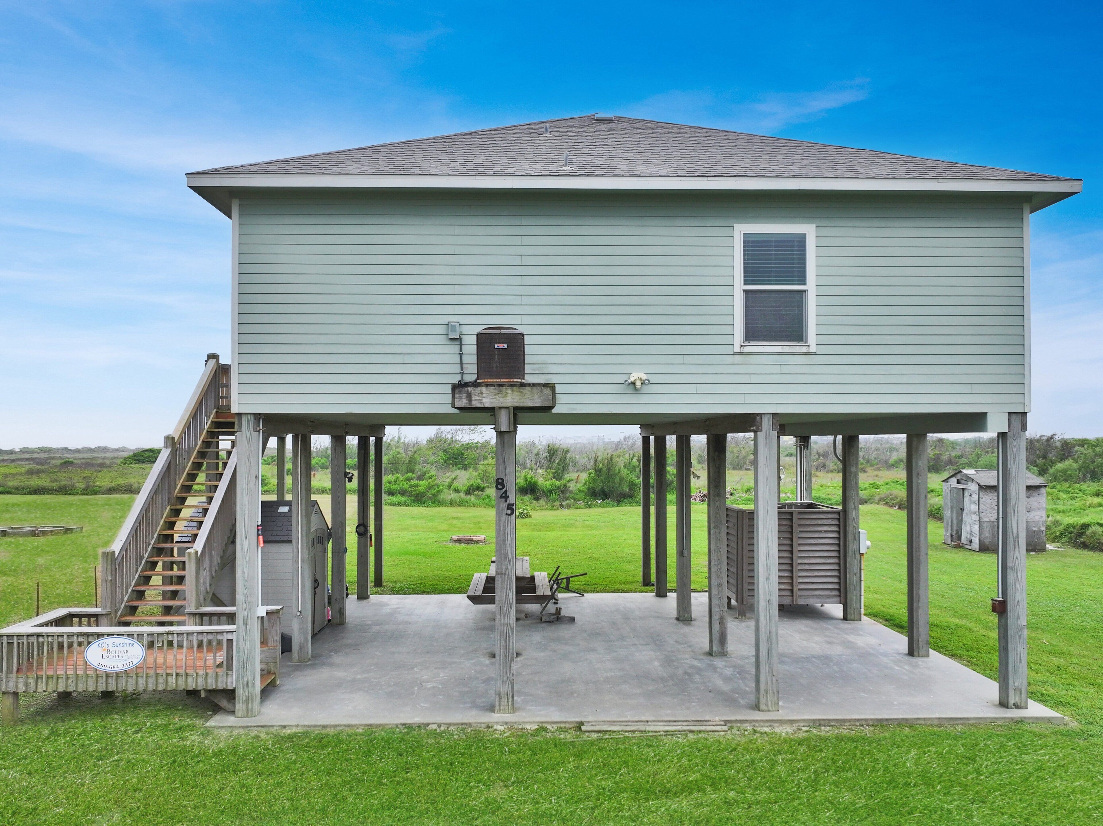 A two-story house with a covered patio, a staircase, and a small shed in the background.